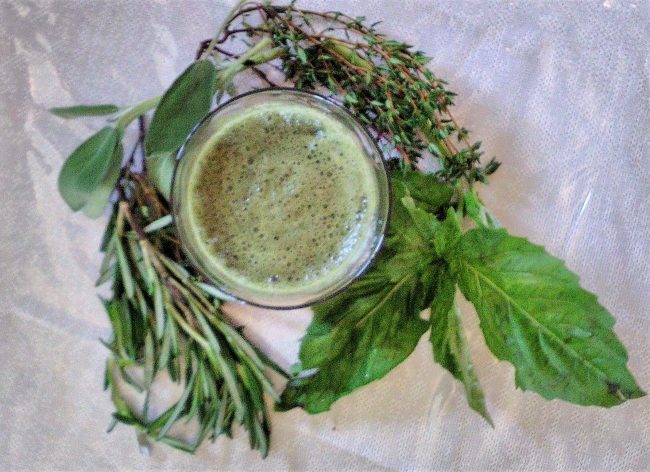 green smoothie surrounded by fresh sage, basil, thyme, and rosemary leaves