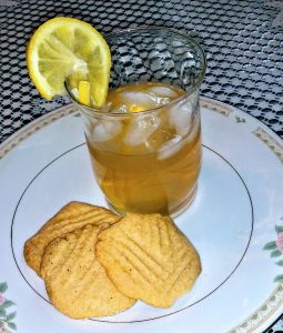 Small glass of lemonade with a lemon slice on the glass sits on a white plate with 3 cookies.