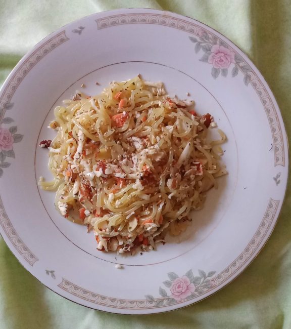 Noodle cabbage salad with slivered almonds centered on a white plate with rose trim border.