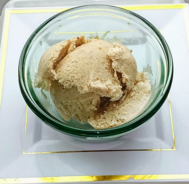 Ice cream in a green glass bowl on a square white plate with gold borders.